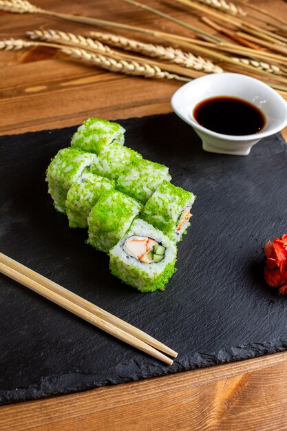 Une vue de face des rouleaux de poisson de couleur verte remplis de légumes en tranches de riz avec de la sauce noire du poisson au Japon