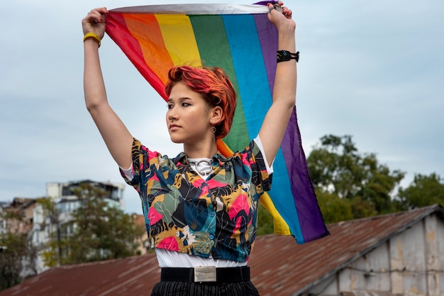 Vue de face rousse personne non binaire tenant un drapeau lgbt