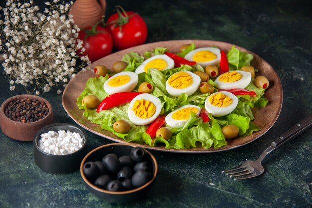 Vue de face de la salade aux œufs se compose d'olives et de salade verte sur fond bleu foncé