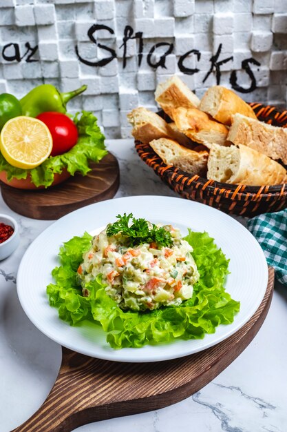 Vue de face salade capitale sur la laitue dans une assiette avec une tranche de citron et de tomate et du pain dans un panier