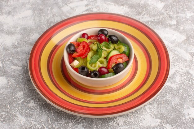 Vue de face salade de légumes frais avec des tranches de concombres tomates olive et fromage blanc à l'intérieur de la plaque sur la surface grise salade de légumes repas collation photo