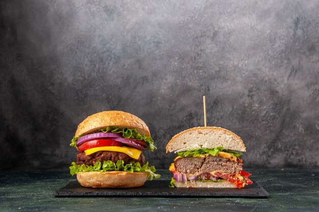 Vue de face de sandwichs savoureux entiers coupés sur un plateau noir sur une surface de couleur sombre