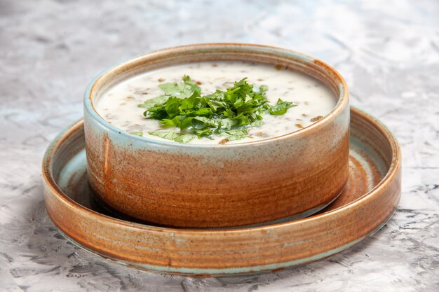 Vue de face savoureuse soupe au yaourt dovga avec des légumes verts sur un plat blanc clair de soupe au lait de table