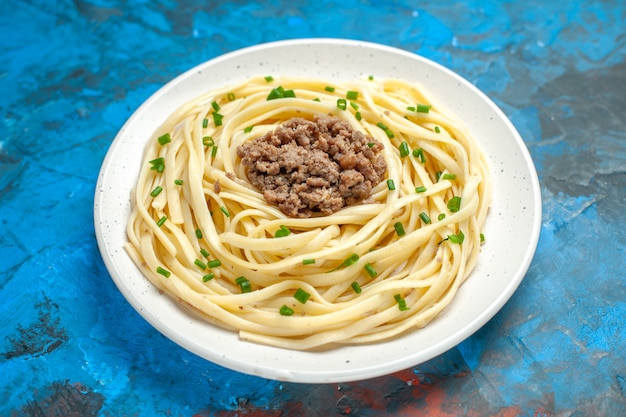 Vue de face de savoureuses pâtes italiennes avec des légumes verts et de la viande hachée sur la couleur du plat de nourriture de repas de pâte bleue