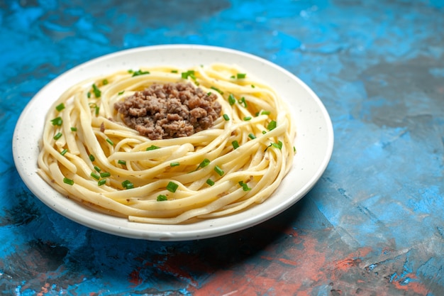 Vue de face de savoureuses pâtes italiennes avec des légumes verts et de la viande hachée sur la couleur du plat de repas de pâte bleue