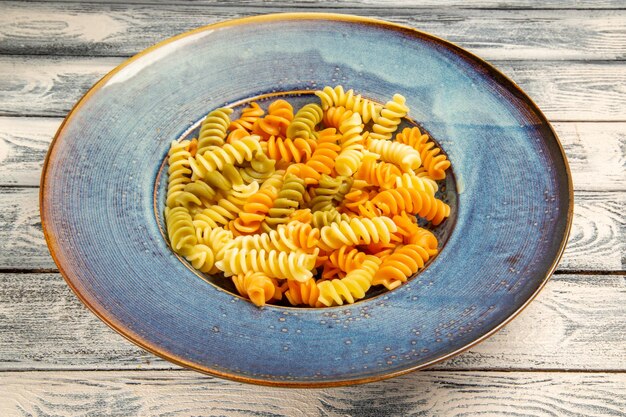 Vue de face de savoureuses pâtes italiennes pâtes en spirale cuites inhabituelles sur un bureau en bois gris cuisinant un plat de pâtes de pâte à dîner