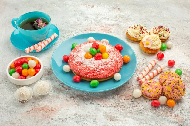 Vue de face savoureux gâteau rose avec de délicieux gâteaux aux biscuits et thé sur fond blanc goodie arc-en-ciel bonbons dessert couleur gâteau