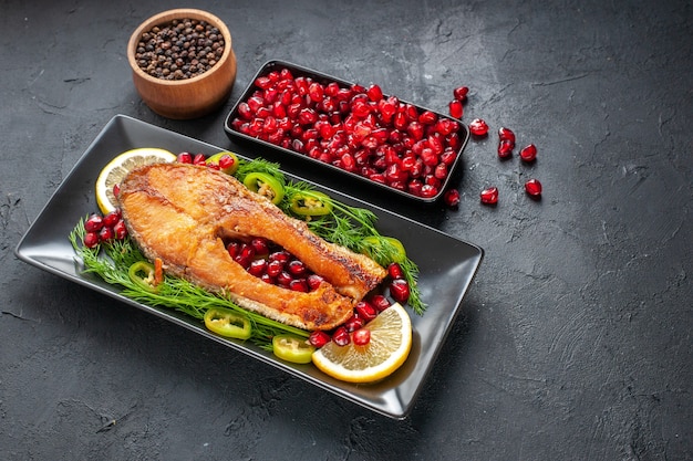 Vue de face savoureux poisson cuit avec des grenades et des tranches de citron à l'intérieur de la casserole sur fond gris foncé plat couleur nourriture photo viande santé fruits de mer