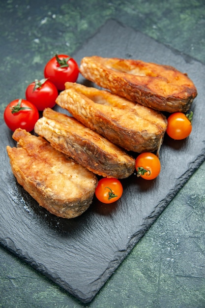 Vue de face savoureux poisson frit avec des tomates sur une surface sombre repas salade alimentaire viande poivrée fruits de mer plat de cuisson frire