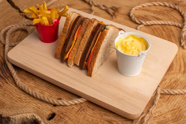 Vue de face savoureux sandwich au pain grillé avec jambon au fromage avec frites crème sure sur bois