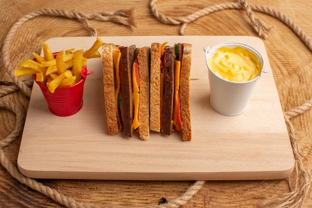 Vue de face savoureux sandwich au pain grillé avec jambon au fromage avec frites crème sure sur bois