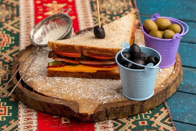 Vue de face savoureux sandwich toast avec du jambon au fromage à l'intérieur avec des olives de farine sur bleu