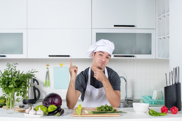 Vue de face se demandait un jeune cuisinier en uniforme pointant sur un placard dans une cuisine moderne