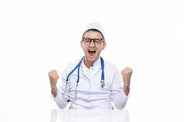Vue de face se réjouissant médecin de sexe masculin en costume médical assis derrière un bureau
