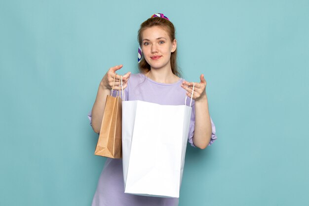 Une vue de face séduisante femme en robe-chemise bleue tenant des paquets d'achat sur bleu