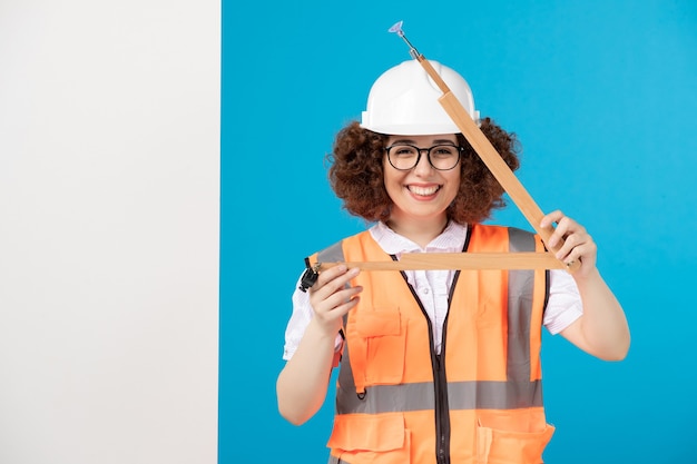 Vue de face souriant constructeur féminin en uniforme avec outil en bois sur bleu