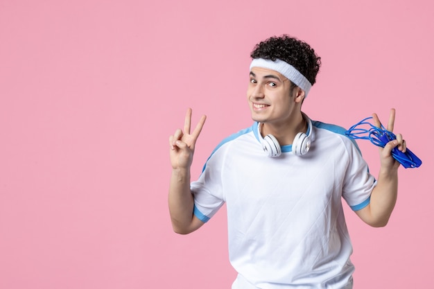 Vue de face souriant jeune homme en vêtements de sport avec corde à sauter