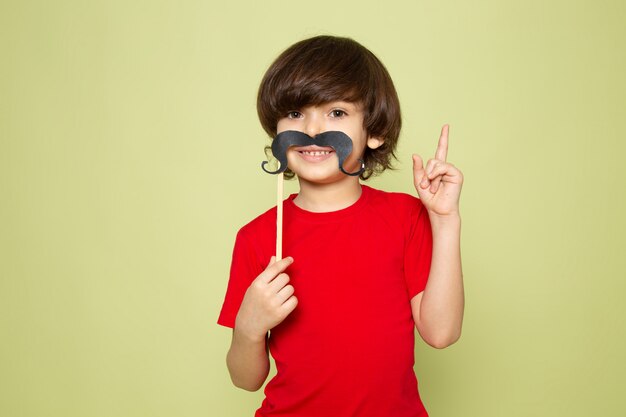 Une vue de face souriant mignon garçon en t-shirt rouge et moustache sur l'espace de couleur pierre