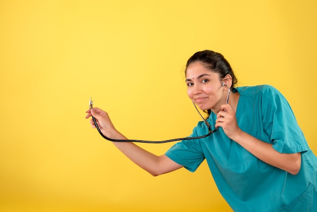 Vue de face sourit jeune femme médecin avec stéthoscope sur fond jaune