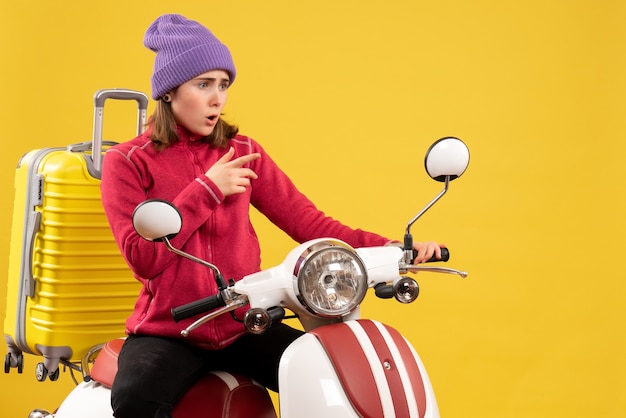 Vue de face surpris jeune fille sur un cyclomoteur en montrant quelque chose