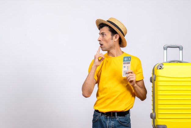 Vue de face surpris jeune homme en t-shirt jaune debout près de la valise jaune en regardant quelque chose