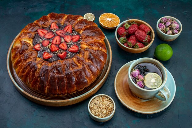 Vue de face de la tarte aux fraises avec tasse de thé sur une surface bleu foncé