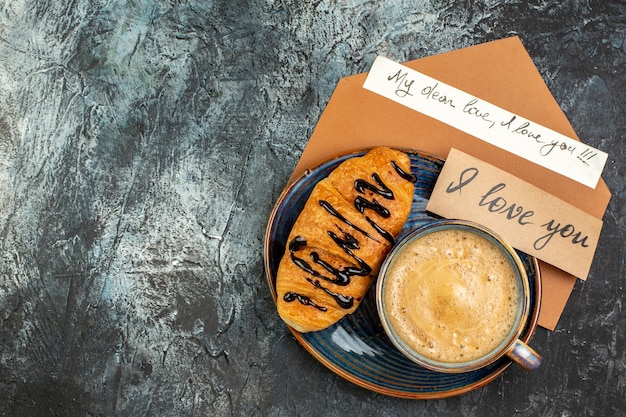 Vue de face d'une tasse de café et d'un délicieux croissant frais pour un bien-aimé sur une surface sombre