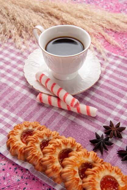 Vue de face tasse de thé avec des biscuits et des bonbons de bâton sur le bureau rose biscuit biscuit sucré