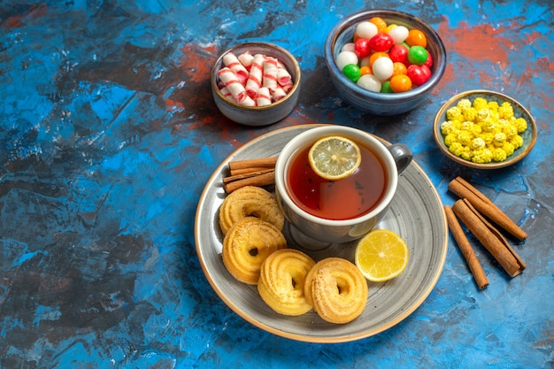 Vue de face tasse de thé avec des biscuits et des bonbons sur le thé de bonbons de biscuit de table bleu