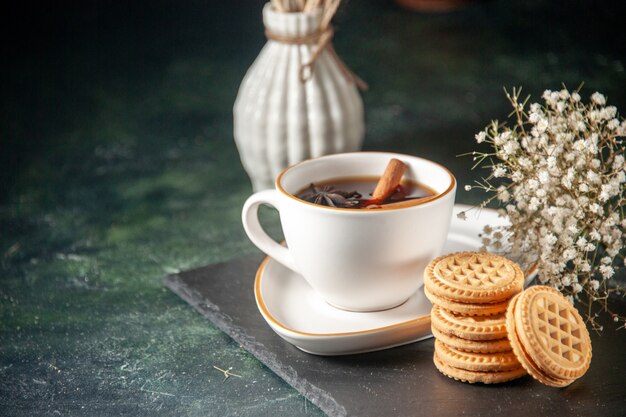 Vue de face tasse de thé avec des biscuits sucrés sur la surface sombre du pain verre cérémonie boisson petit-déjeuner sucré gâteau couleur sucre matin