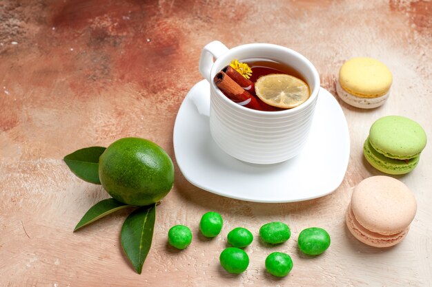 Vue de face tasse de thé avec bonbons et macarons sur table marron clair biscuit citron thé