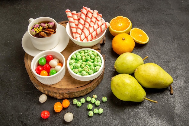 Vue de face tasse de thé avec bonbons poires et mandarines sur espace sombre