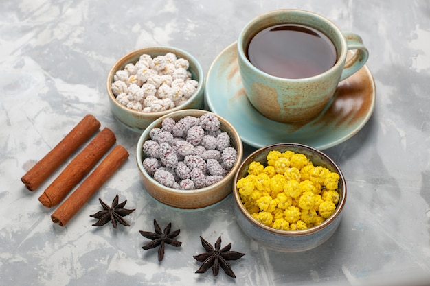 Vue de face tasse de thé avec des bonbons de sucre et de cannelle sur une surface blanche