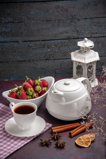 Vue de face tasse de thé avec de la cannelle et des fraises sur une surface sombre boire du thé couleur fruits