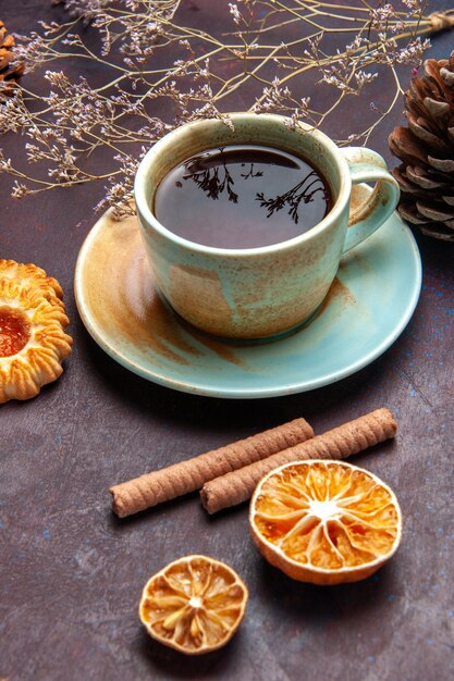 Vue de face tasse de thé avec des cookies sur un espace sombre