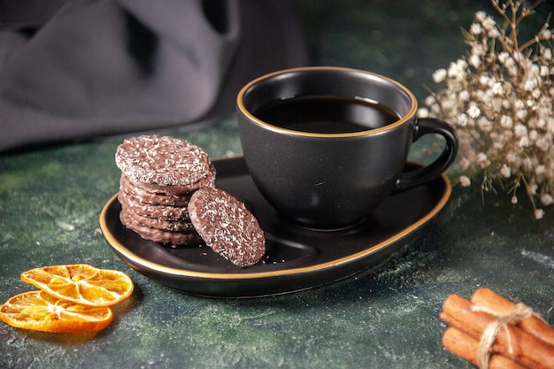 Vue de face tasse de thé dans une tasse noire et une assiette avec des biscuits sur la surface sombre couleur sucre cérémonie verre petit déjeuner gâteau dessert
