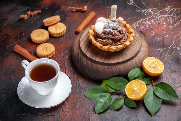 Vue de face tasse de thé avec un délicieux petit gâteau sur fond sombre