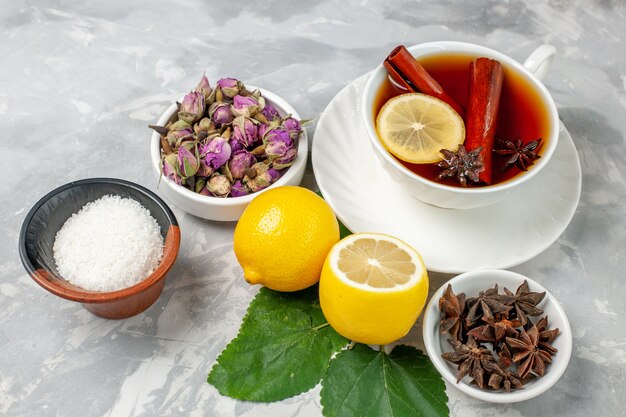 Vue de face tasse de thé avec des fleurs et du citron sur une surface blanche