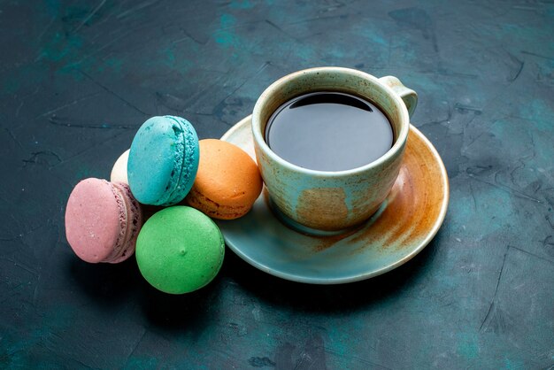 Vue de face tasse de thé avec des macarons français sur backgruond bleu foncé cuire gâteau tarte au sucre thé sucré