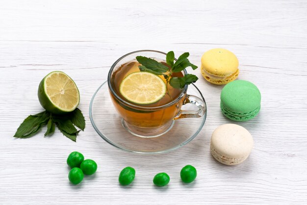 Une vue de face tasse de thé avec macarons français et citron sur blanc, biscuit gâteau au thé