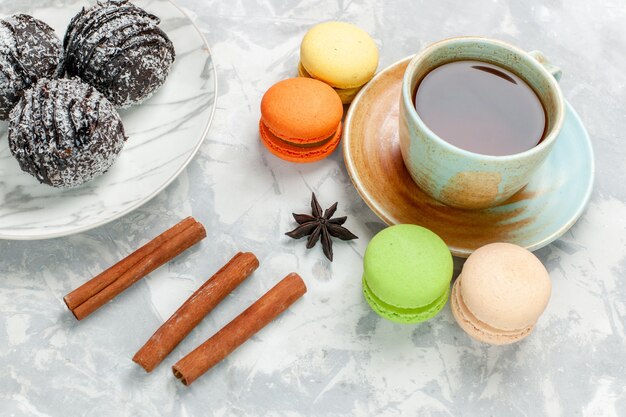 Vue de face tasse de thé avec des macarons gâteaux au chocolat et cannelle sur bureau blanc cuire gâteau biscuit sucre tarte sucrée