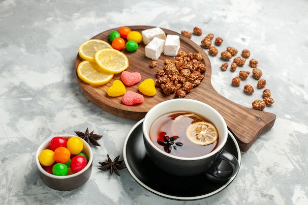 Vue de face tasse de thé avec des noix et des bonbons sur une surface blanche