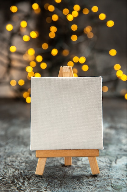 Photo gratuite vue de face toile blanche sur chevalet en bois lumières de noël sur dark