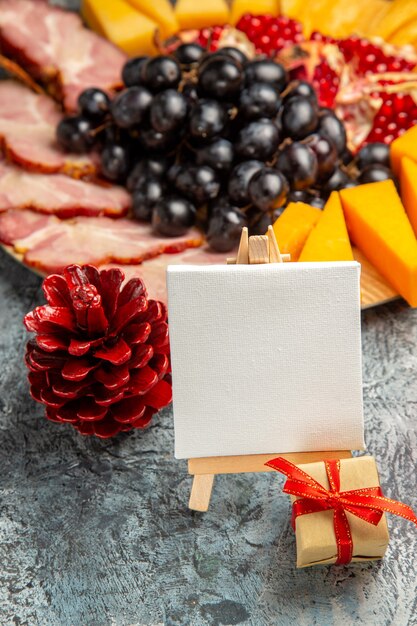 Vue de face toile blanche sur chevalet en bois raisins morceaux de fromage tranches de viande sur plaque de bois détails de noël sur noir