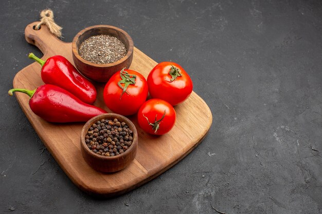 Vue de face des tomates fraîches avec des assaisonnements et du poivron rouge sur un espace sombre