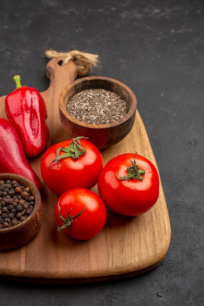 Vue de face des tomates rouges fraîches avec des assaisonnements sur l'espace sombre