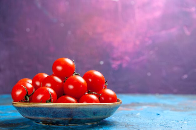 Vue de face des tomates rouges fraîches à l'intérieur de la plaque sur la table bleue