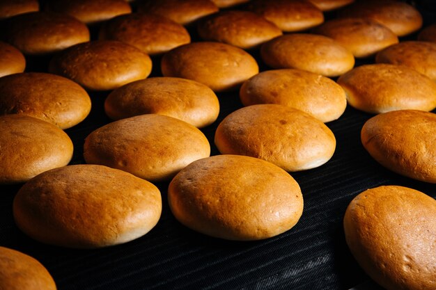 Une vue de face tout le pain rond cuit sur la table noire à l'intérieur de la pâte à pain alimentaire d'usine