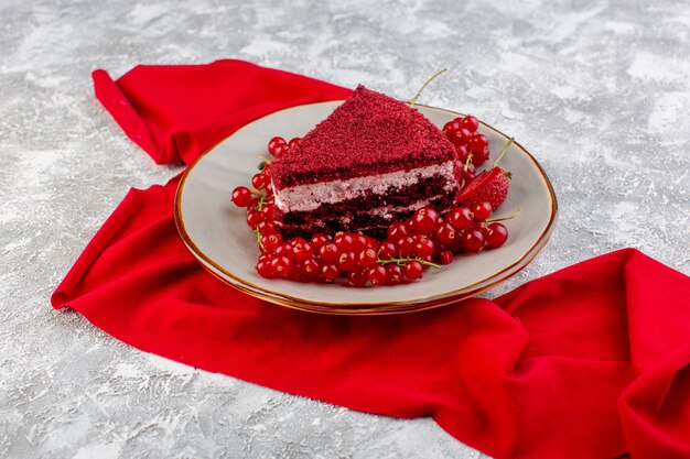 Vue de face tranche de gâteau rouge morceau de gâteau aux fruits à l'intérieur de la plaque avec des canneberges fraîches et des fraises sur le thé gris