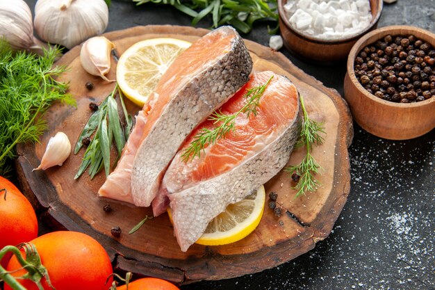 Vue de face des tranches de poisson frais avec des tomates et des tranches de citron sur un plat de fruits de mer de couleur brute foncée photo nourriture à base de viande